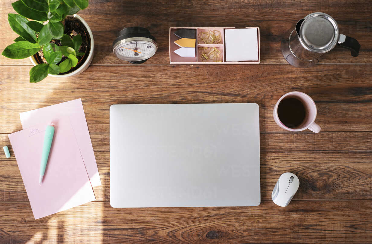 Closed laptop, coffee mug and other utensils on desk at home office, top view