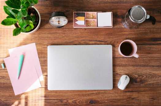 Closed laptop, coffee mug and other utensils on desk at home office, top view